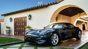 A black Karma Revero GT plug-in hybrid electric vehicle (PHEV) parked on the brick driveway of a luxury home