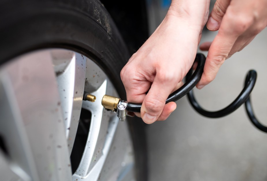 Closeup of hands holding the end of a compressor hose, filling up a tire PSI.