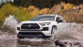 A white 2023 Toyota RAV4 is driving through the water.