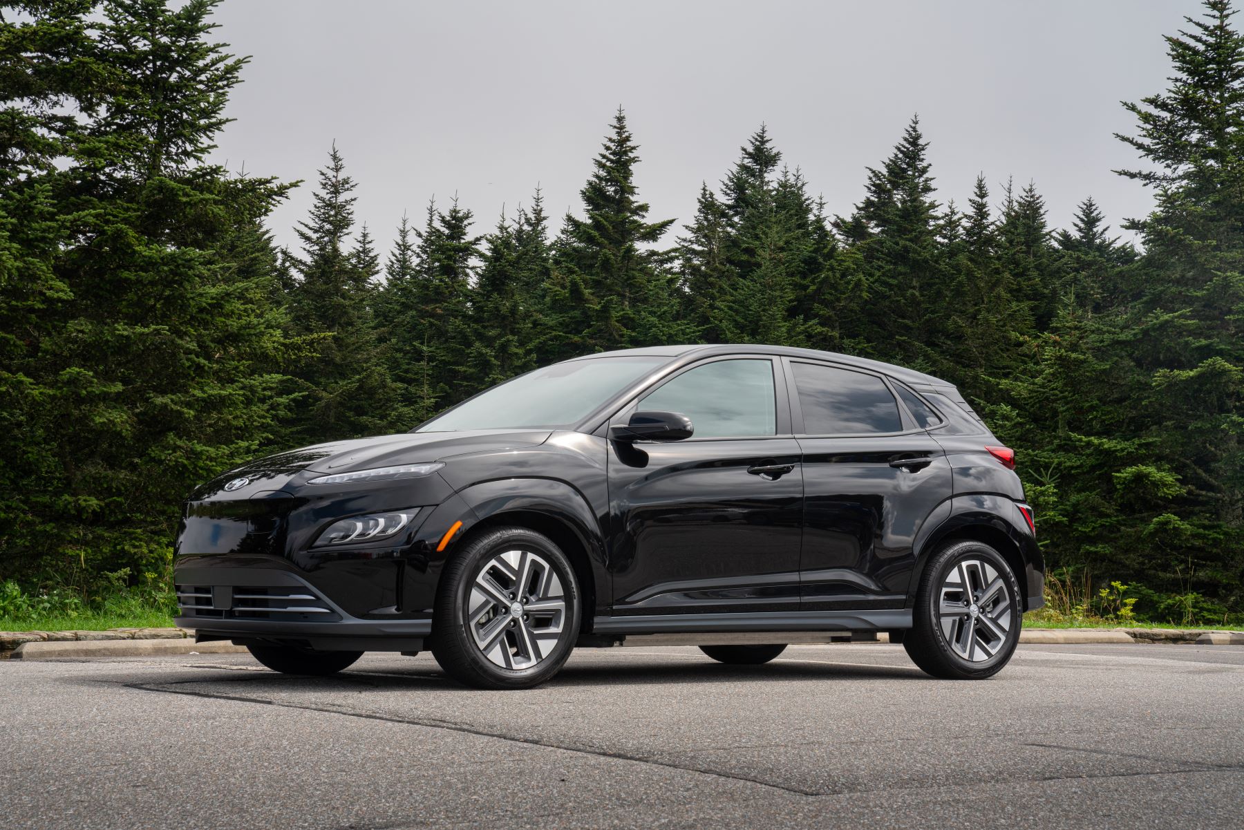 A black 2023 Hyundai Kona Electric all-electric (EV) compact SUV model parked near a forest of evergreen trees