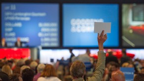 A person holding up a paddle at an action similar to what you would do when you buy a vehicle from a Government Auction.