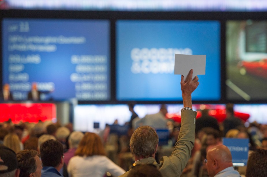 A person holding up a paddle at an action similar to what you would do when you buy a vehicle from a Government Auction. 