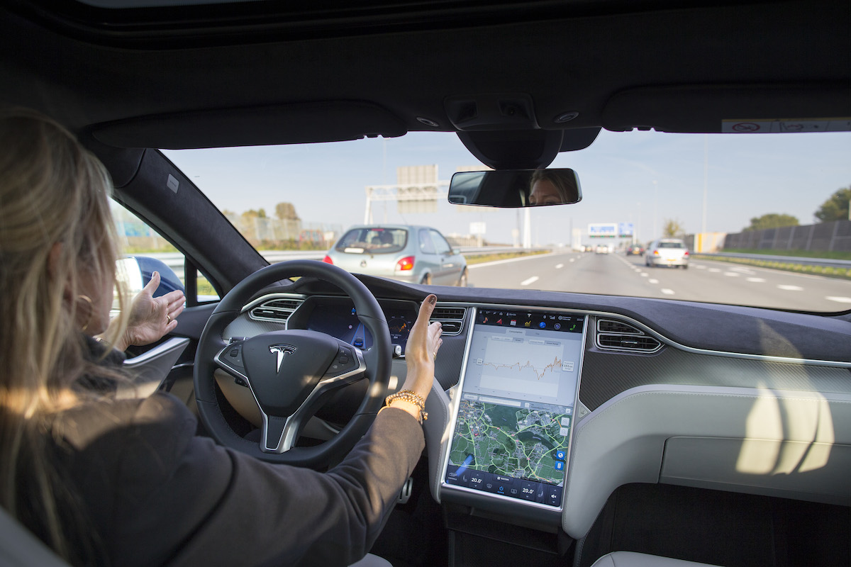 An employee drives a Tesla Model S equipped with Autopilot down a highway with her hands off the wheel.