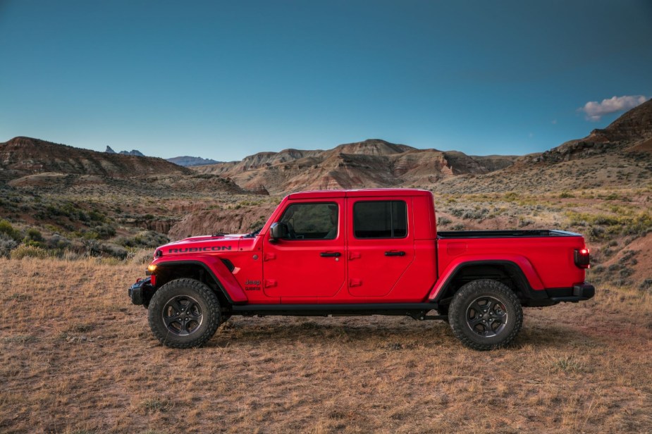 A side profile shot of a red 2023 Jeep Gladiator Rubicon midsize pickup truck parked in the wilderness