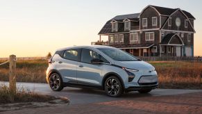 A sky blue 2022 Chevy Bolt EV hatchback model parked before a brick walkway