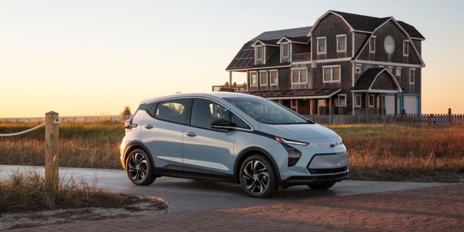 A sky blue 2022 Chevy Bolt EV hatchback model parked before a brick walkway