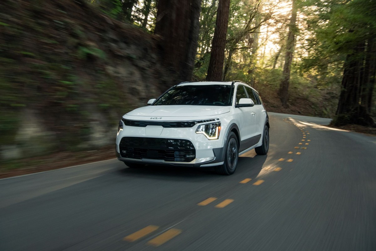 A white 2023 Kia Niro EV electric compact SUV model driving on a winding forest highway