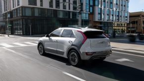 A white 2023 Kia Niro EV electric compact SUV model driving through an urban city near a set of streetlights