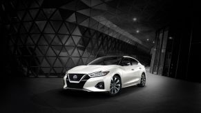 A white 2023 Nissan Maxima midsize sedan promotional shot surrounded by a grayed out interior of a glass building