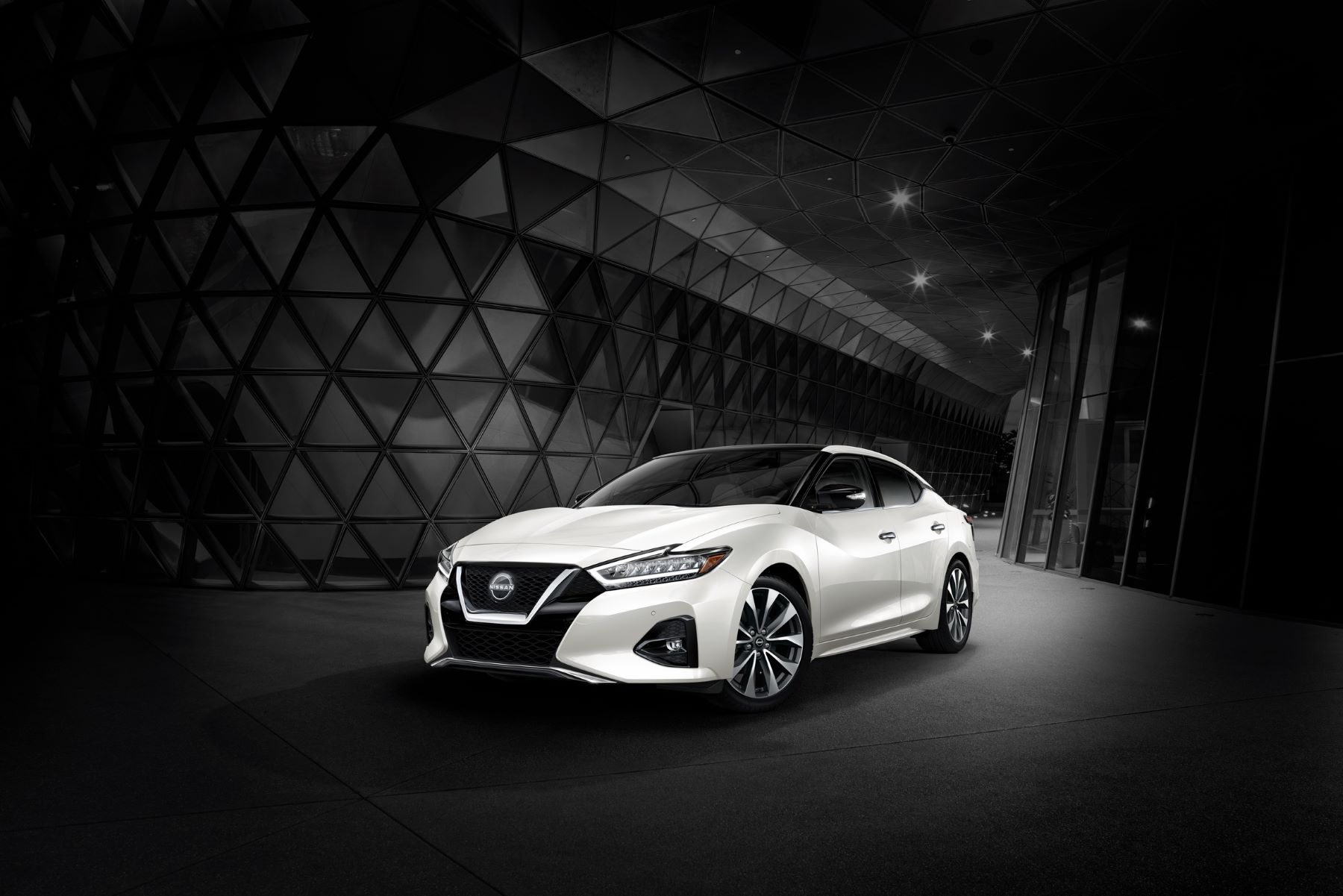 A white 2023 Nissan Maxima midsize sedan promotional shot surrounded by a grayed out interior of a glass building