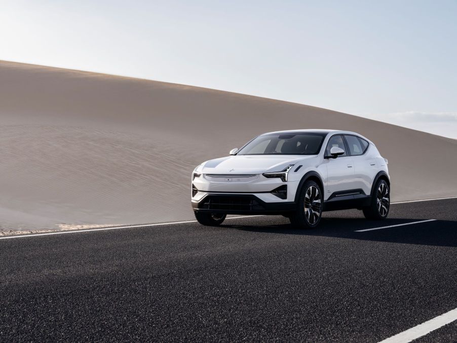 A white Polestar 3 all-electric luxury SUV on a shiny black highway near a sand dune