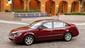 A dark red 2006 Nissan Altima midsize sedan model parked on a cobblestone villa