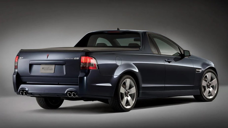 The rear end of a dark blue two-door Pontiac G8 Sport Truck compact vehicle with its pickup bed visible, a simple gray background.