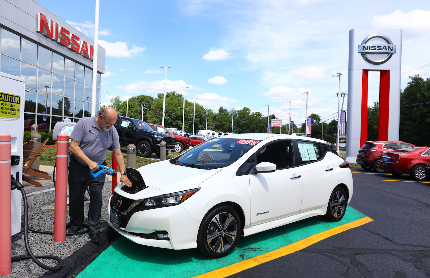 White Nissan Leaf EV parked at a dealership, charging.