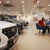 A row of Hyundai EVs parked inside a dealership, a table of customers speak with a salesperson in the background.