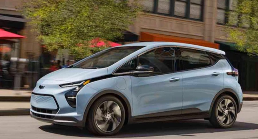 A blue 2023 Chevy Bolt EV electric hatchback is driving on the road.