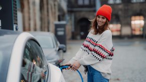 A woman in an orange hat plugs a rapid charger cable in to the port of her Tesla sedan.