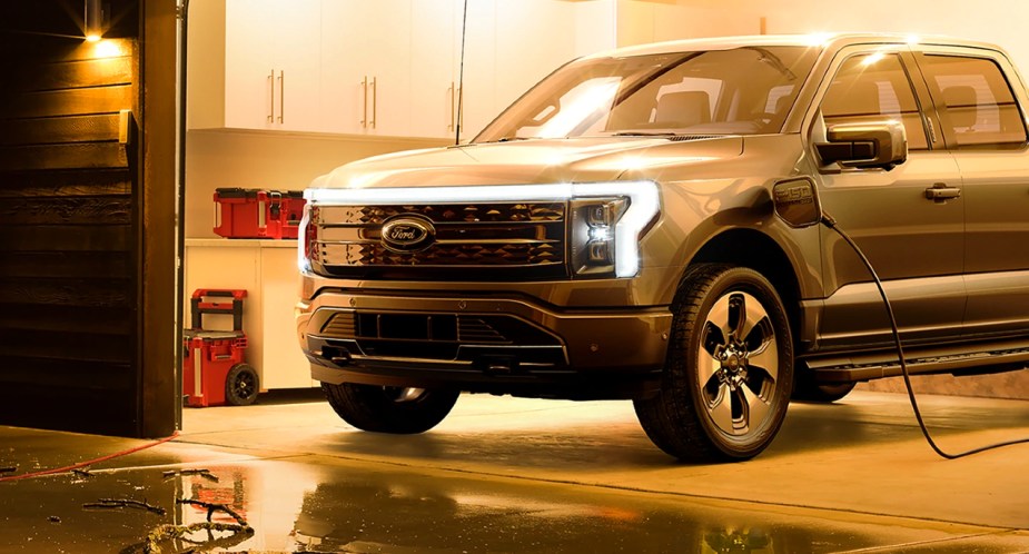 A gray 2023 Ford F-150 lightning electric pickup truck is charging in a garage.