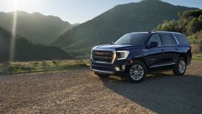 A 2023 GMC Yukon SLT full-size SUV model parked on a dirt plain as the sun glares over grassy mountains