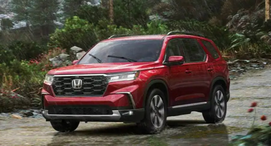 A red 2023 Honda Pilot midsize SUV is driving off-road.