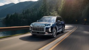 A blue 2023 Hyundai Palisade midsize SUV is driving on the road.