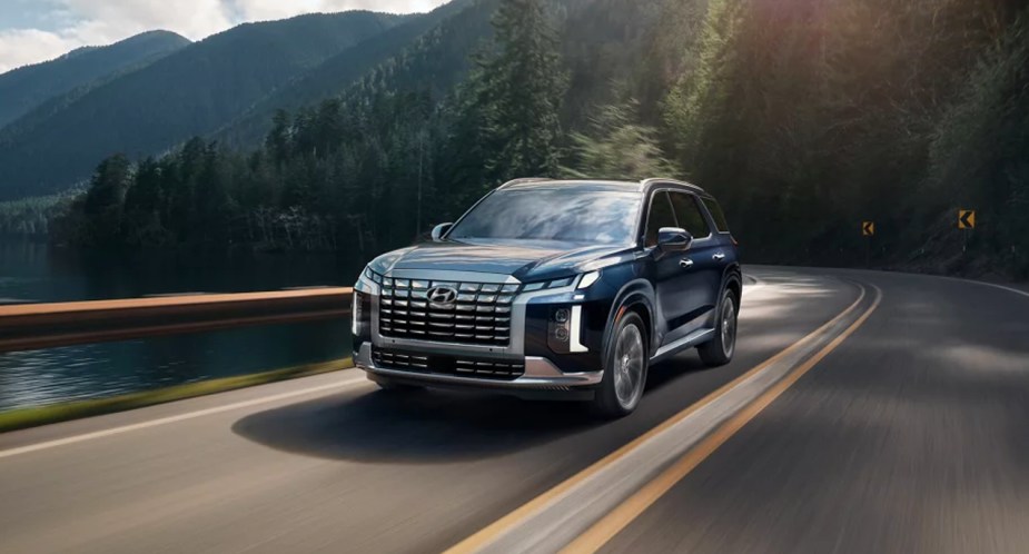 A blue 2023 Hyundai Palisade midsize SUV is driving on the road. 