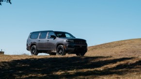 A gray Wagoneer by Jeep driving along an off-road course, a ridge line visible in the background.