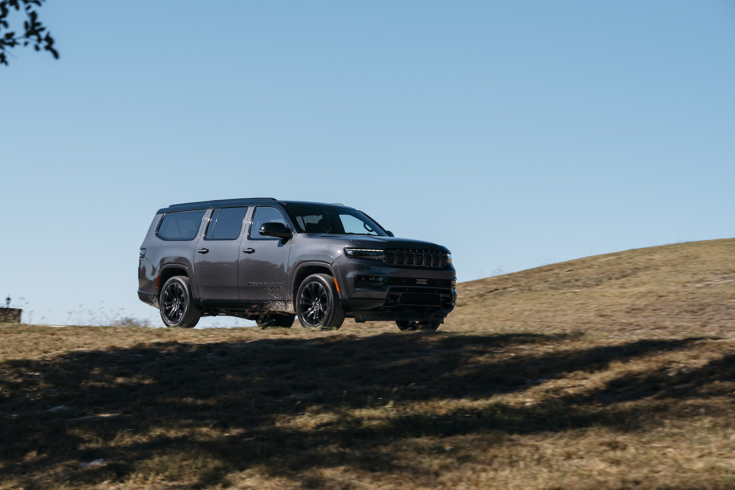 A gray Wagoneer by Jeep driving along an off-road course, a ridge line visible in the background.