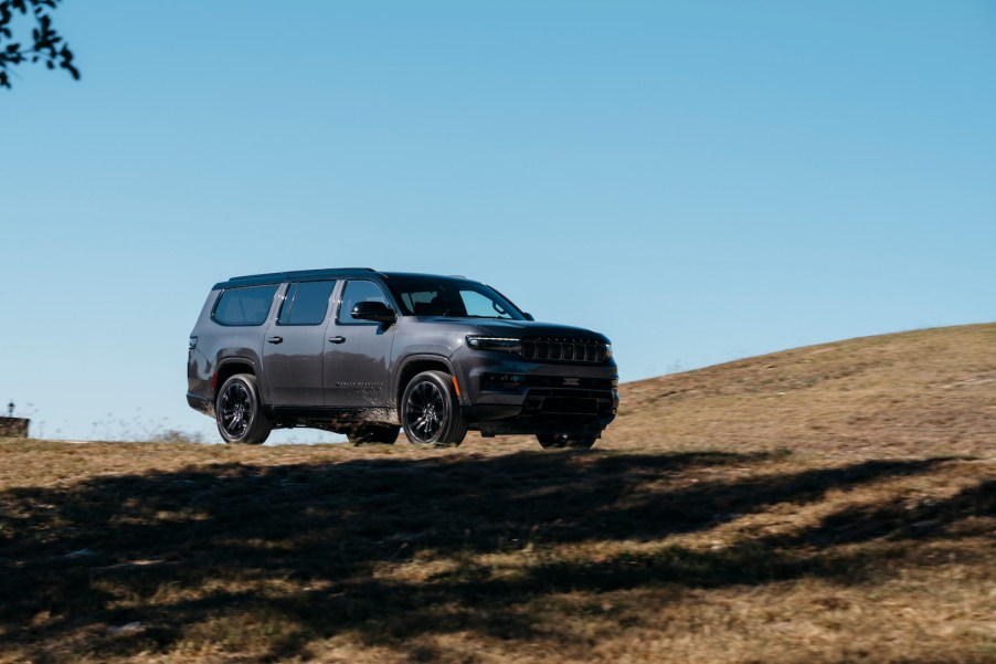 A gray Wagoneer by Jeep driving along an off-road course, a ridge line visible in the background.