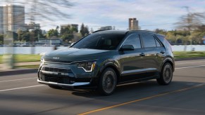 A black 2023 Kia Niro hybrid subcompact SUV is driving on the road.