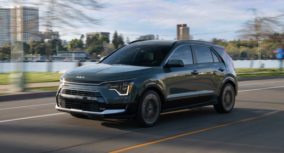 A black 2023 Kia Niro hybrid subcompact SUV is driving on the road.