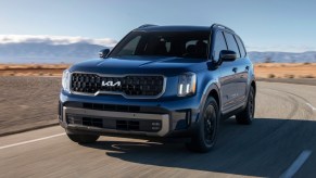 A blue 2023 Kia Telluride midsize SUV is driving on the road.