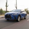 A blue Lexus NX350h hybrid crossover SUV driving through the desert for a promotional photo, cacti visible in the background.