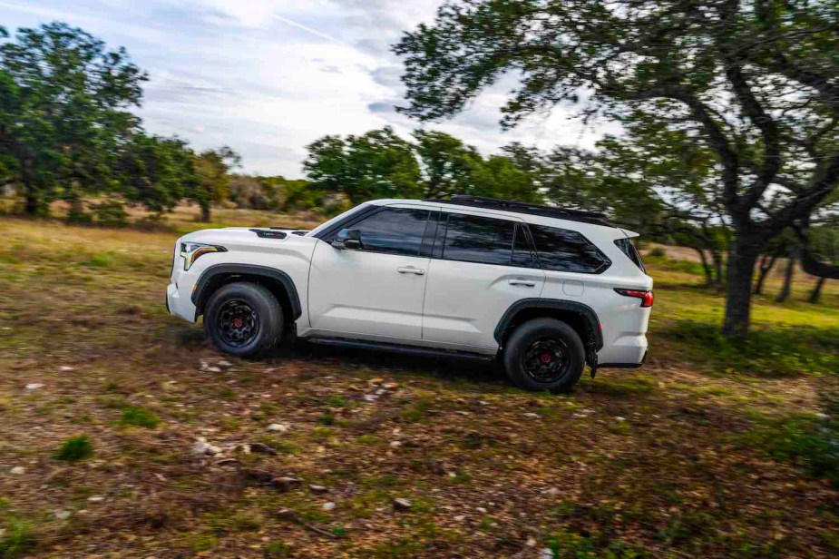 White 2023 Toyota Sequoia TRD Pro speeding along an off-roading trail, a row of trees visible in the background.