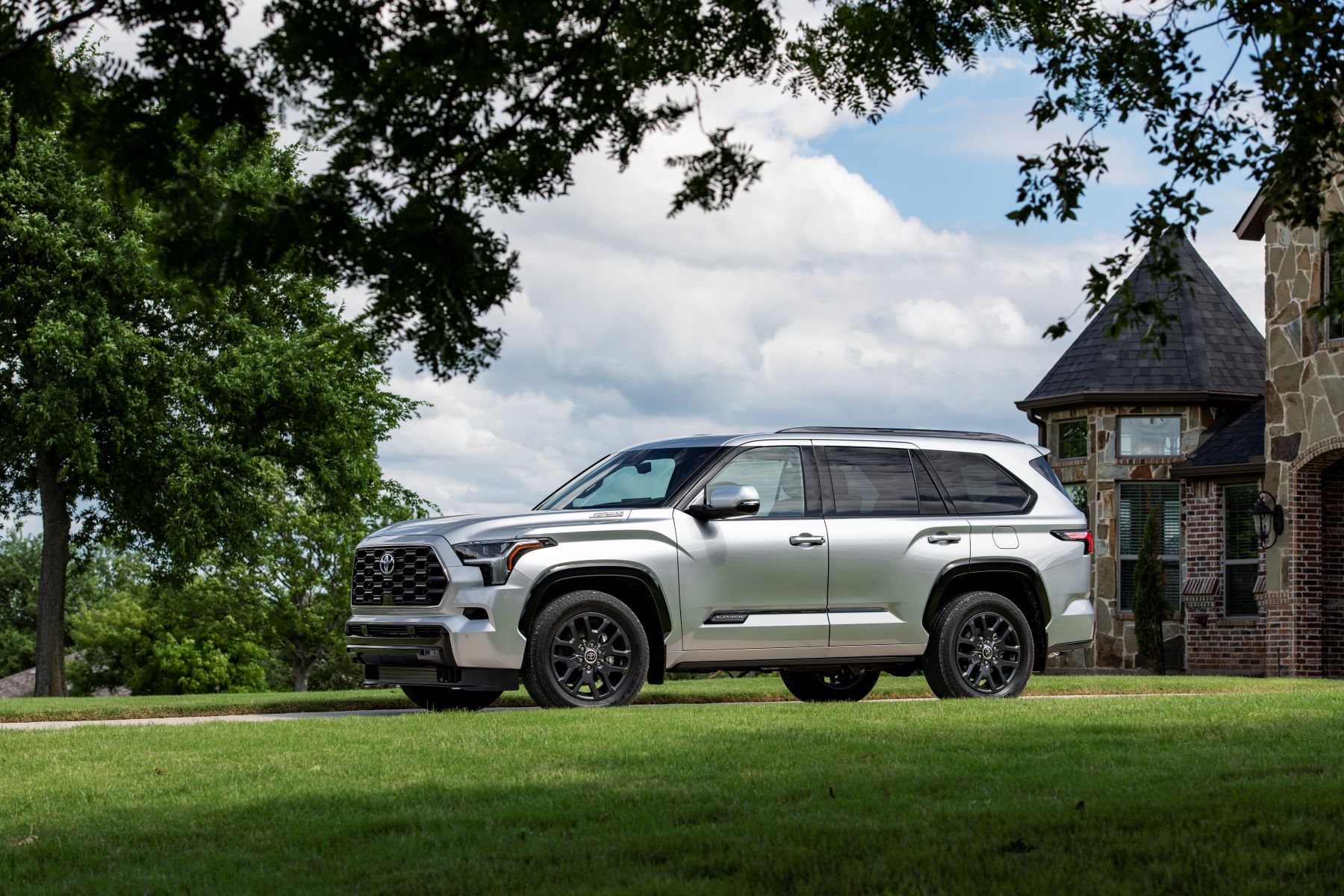 A 2023 Toyota Sequoia full-size SUV in Platinum Silver parked outside a luxury brick mansion