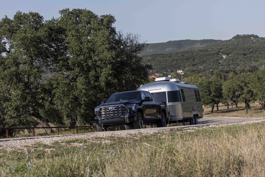 A black Toyota Tundra pickup truck pulls a silver trailer up a remote road, hills visible in the background.