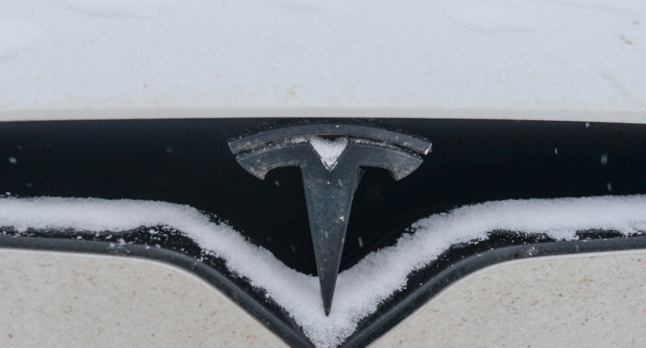 A white Tesla electric vehicle is covered in snow. 