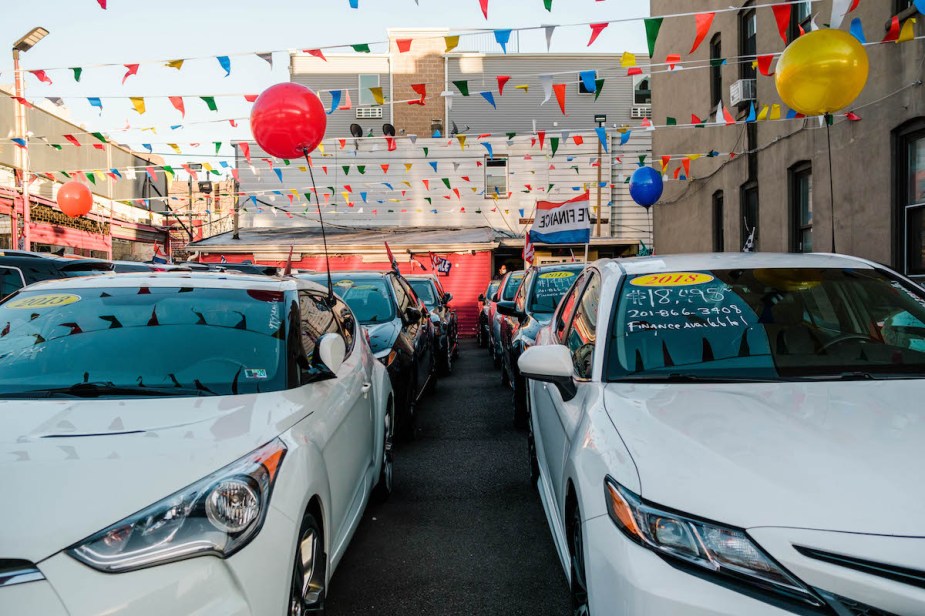 A car dealership with cars, balloons, and flag streamers that could have hidden fees.