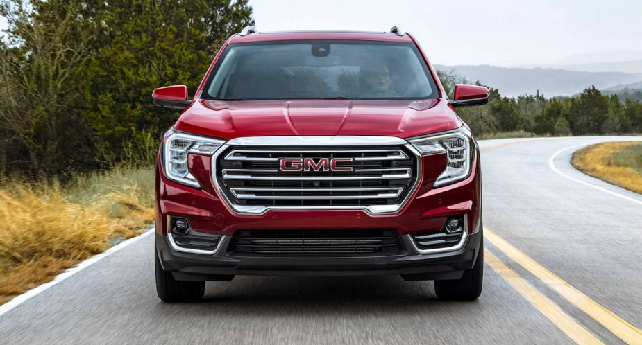 A red 2022 GMC Terrain small SUV is driving on the road. 