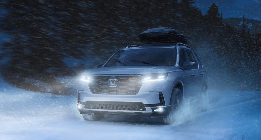 A white 2023 Honda Pilot midsize SUV is driving through the snow.