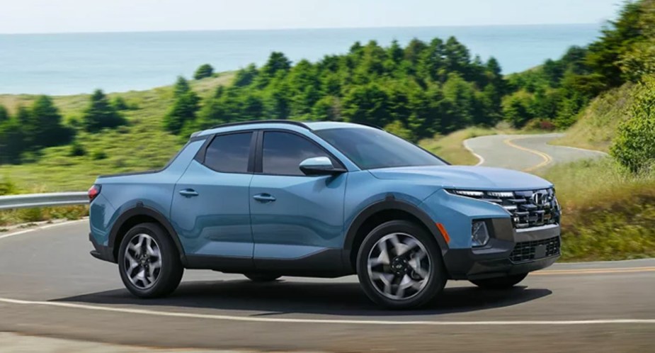 A blue 2023 Hyundai Santa Cruz small pickup truck is driving on the road. 