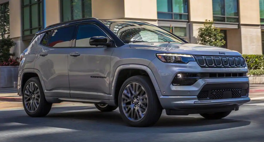 A gray 2023 Jeep Compass small SUV is driving on the road. 