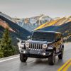 A dark gray Jeep Wrangler Unlimited off-road SUV model driving on a highway near mountains