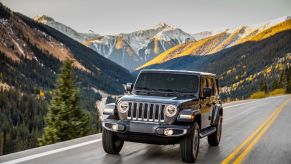 A dark gray Jeep Wrangler Unlimited off-road SUV model driving on a highway near mountains