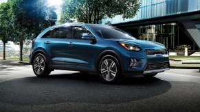 A blue Kia Niro PHEV parked outdoors in front of a large building.