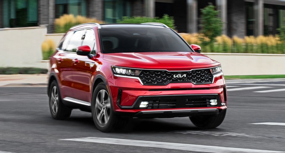 A red Kia Sorento Hybrid midsize hybrid SUV is driving on the road. 