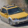 A yellow Subaru Baja compact utility pickup truck built with a midgate driving on a dusty gravel road