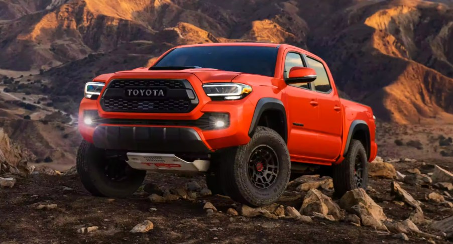 An orange 2023 Toyota Tacoma midsize pickup truck is parked off-road.