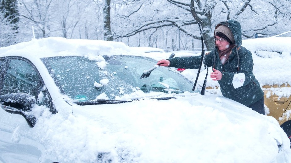 Driver scraping snow and ice from car, highlighting button to defrost ice from car windshield very fast