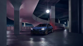 A blue 2023 Toyota Camry Hybrid midsize sedan model with its headlights on in a parking garage at night